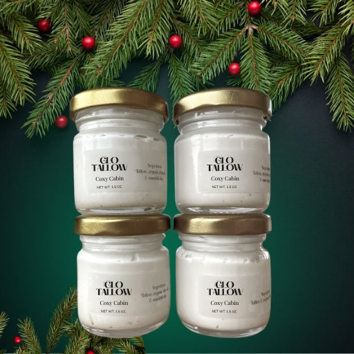 Four jars of Glo Tallow Cozy Cabin tallow balm on a green background with Christmas tree branches.