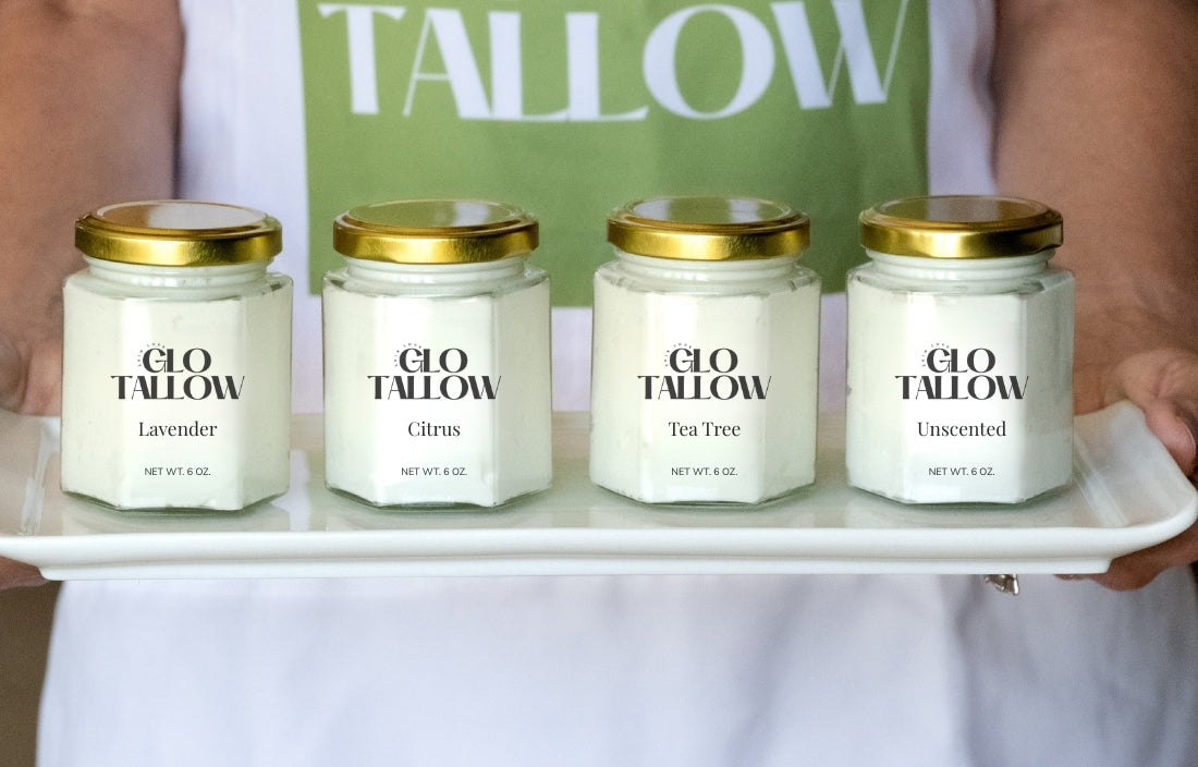 Four jars of Glo Tallow candles on a tray held by a person wearing a white shirt with 'TALLOW' text.