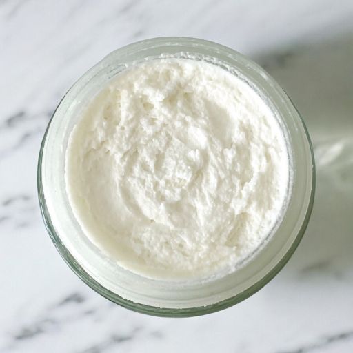 Glass jar filled with white cream on a marble surface